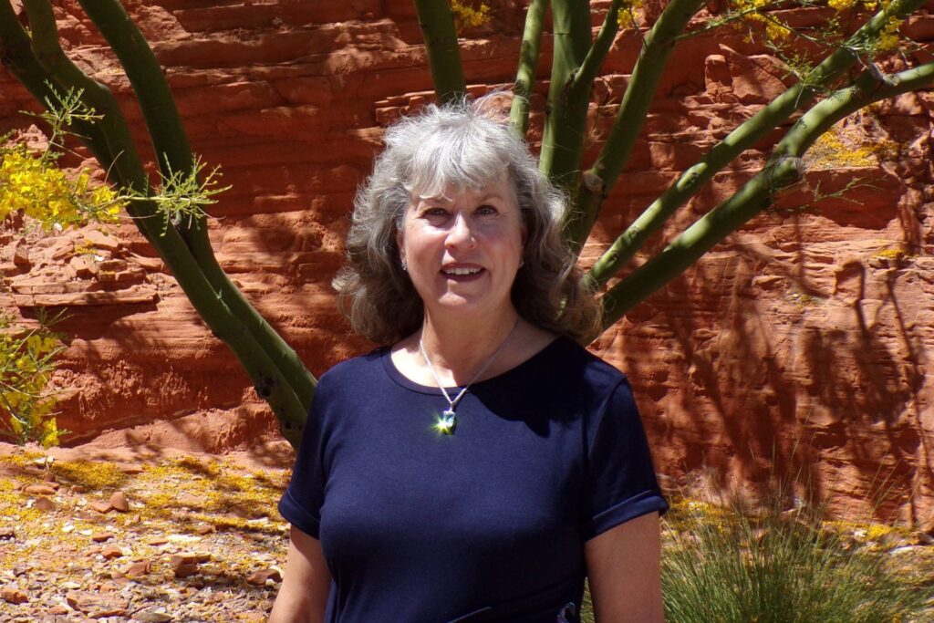 Laura Brooks stands smiling in front of a tree and red rock wall