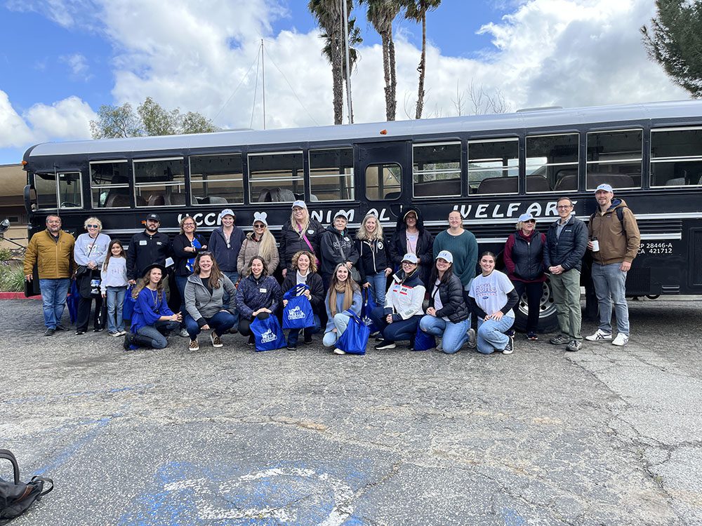 The VCCF Animal Welfare Tour group stands smiling in front of the tour bus