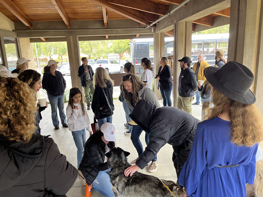 A group of visitors stand around the entrance of the Humane Society of Ventura, some petting a dog