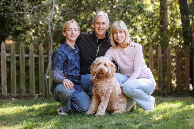 Meryl, Jonathan, and Kyler Chase sitting outside with their goldendoodle Teddi Bear