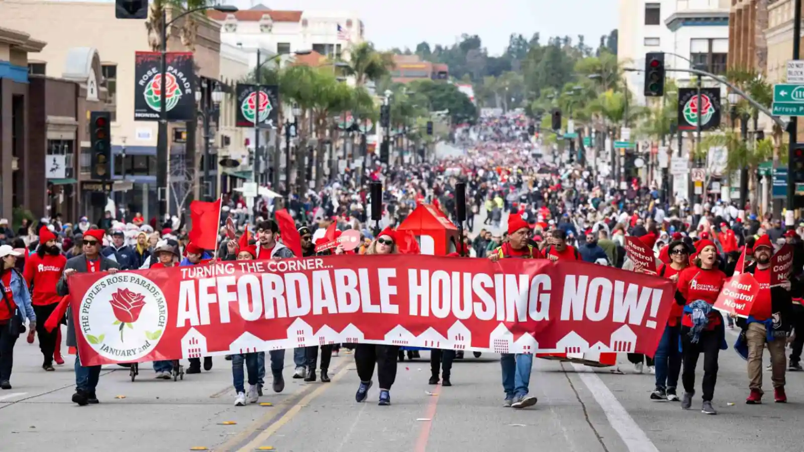 A protest of Pasadena residents wearing red and holding a banner reading "Affordable Housing Now!"