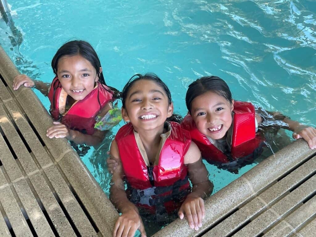 Children smiling and wearing life vests in a pool at the Southeast Ventura County YMCA